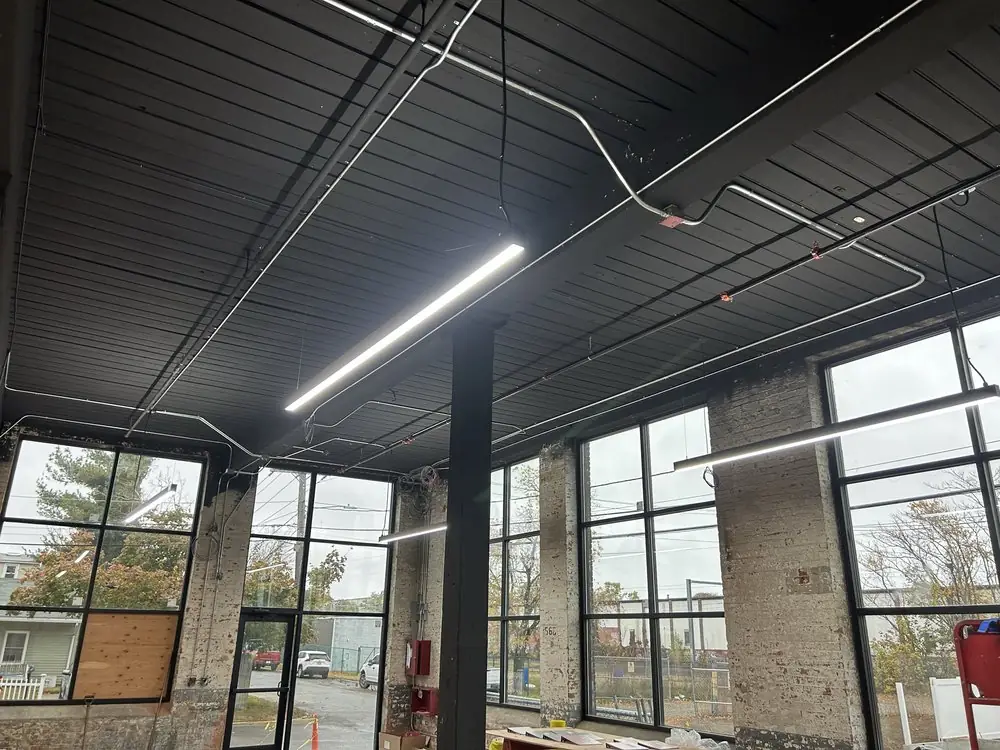 Long LED strip fixtures hung in a commercial space with tall storefront windows