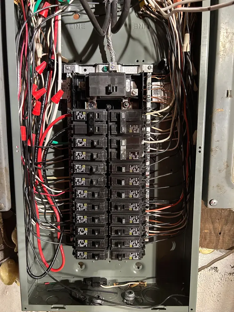 A crowded older panel with red, black and white conductors, opened up for work