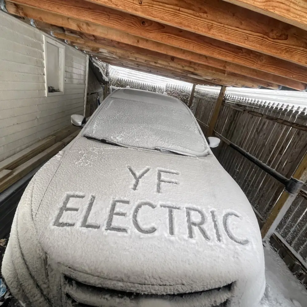 A frosted car under a carport with YF ELECTRIC written in the snow on the hood